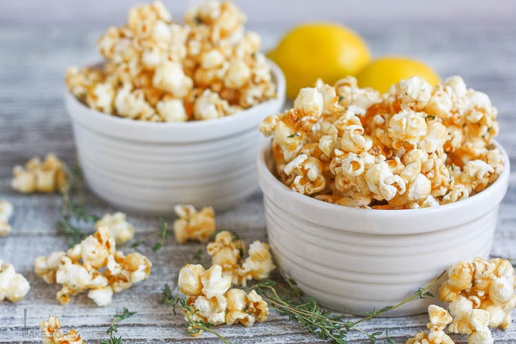 Two bowls of Lemon Thyme Caramel Corn with lemons in the background and fresh thyme and caramel corn scattered around.