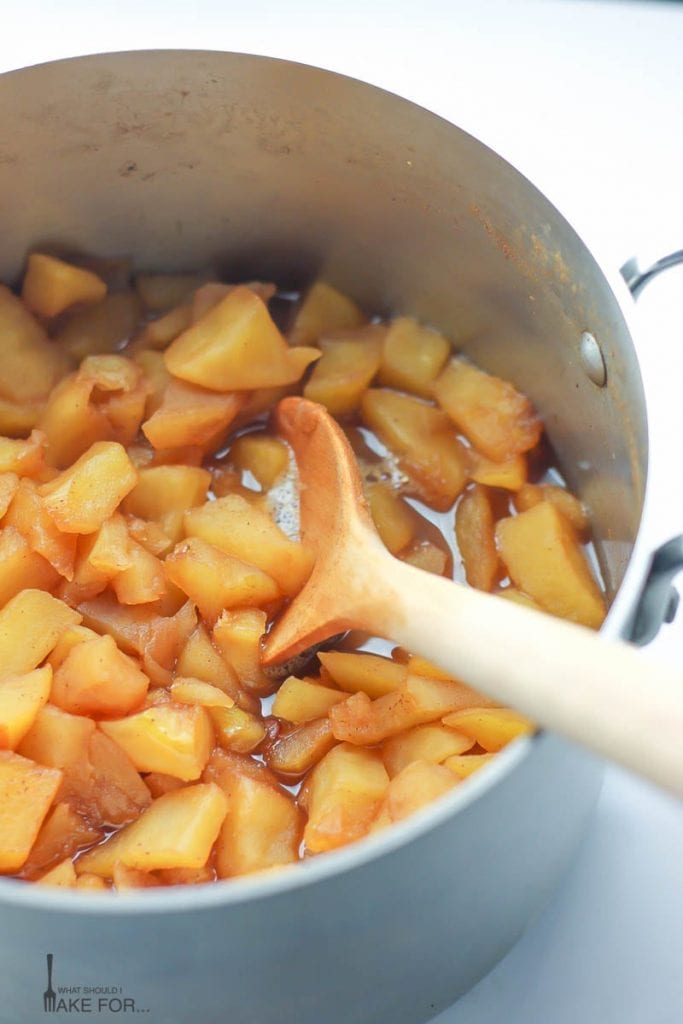Homemade Applesauce cooking in a silver saucepan in chunks stirred with a wooden spoon.