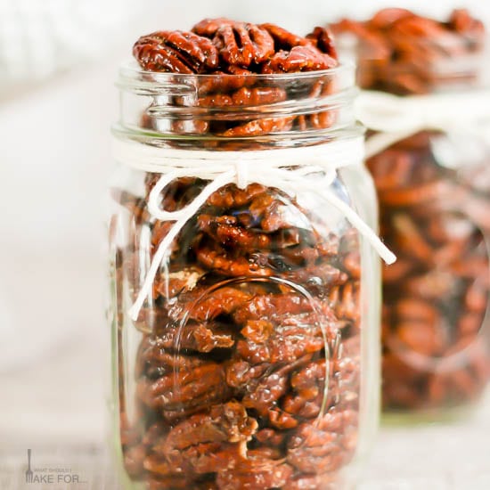 Candied pecans in a mason jar with a white string tied in a bow.
