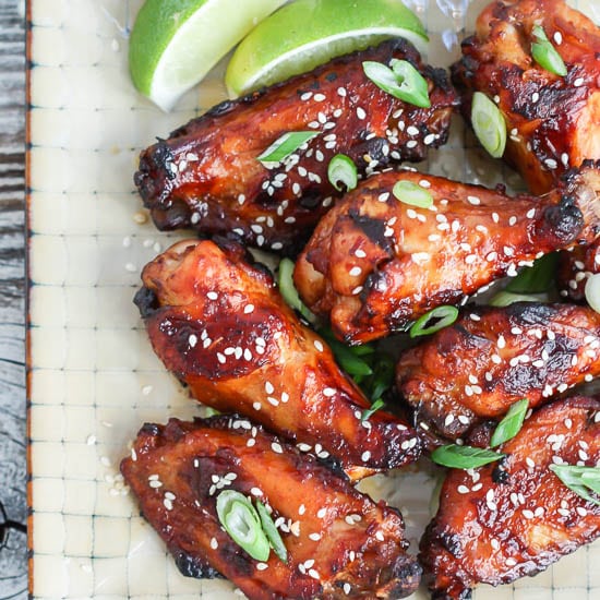 Crispy Asian Chicken Wings served on a square plate, sprinkled with sesame seeds, scallion slices, and lime wedges.