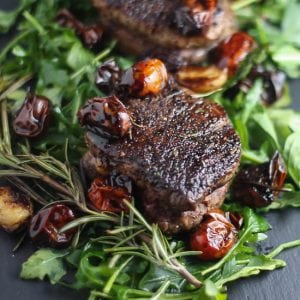 Close up shot of Filet Mignon with Balsamic Tomatoes on a bed of arugula.