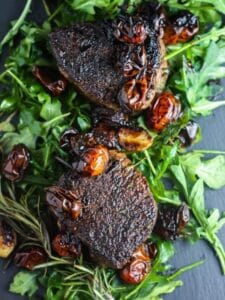 Overhead shot of two Filet Mignons with Balsamic Tomatoes on a bed of arugula.