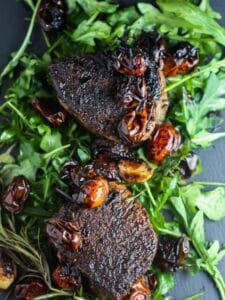 Overhead shot of two Filet Mignons with Balsamic Tomatoes on a bed of arugula.