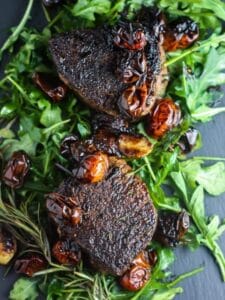 Overhead shot of two Filet Mignons with Balsamic Tomatoes on a bed of arugula.
