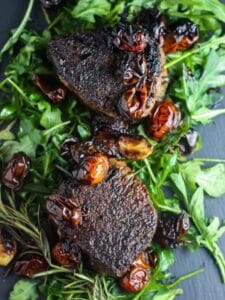 Overhead shot of two Filet Mignons with Balsamic Tomatoes on a bed of arugula.