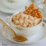 Coconut Rice Pudding with Coconut Caramel Brittle served in a pretty china cup on a saucer with a gold spoon alongside.
