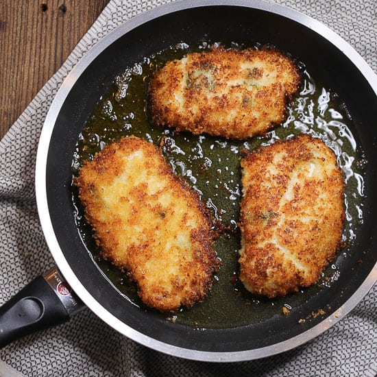 Close up of breaded chicken breasts cooking in a frying pan.