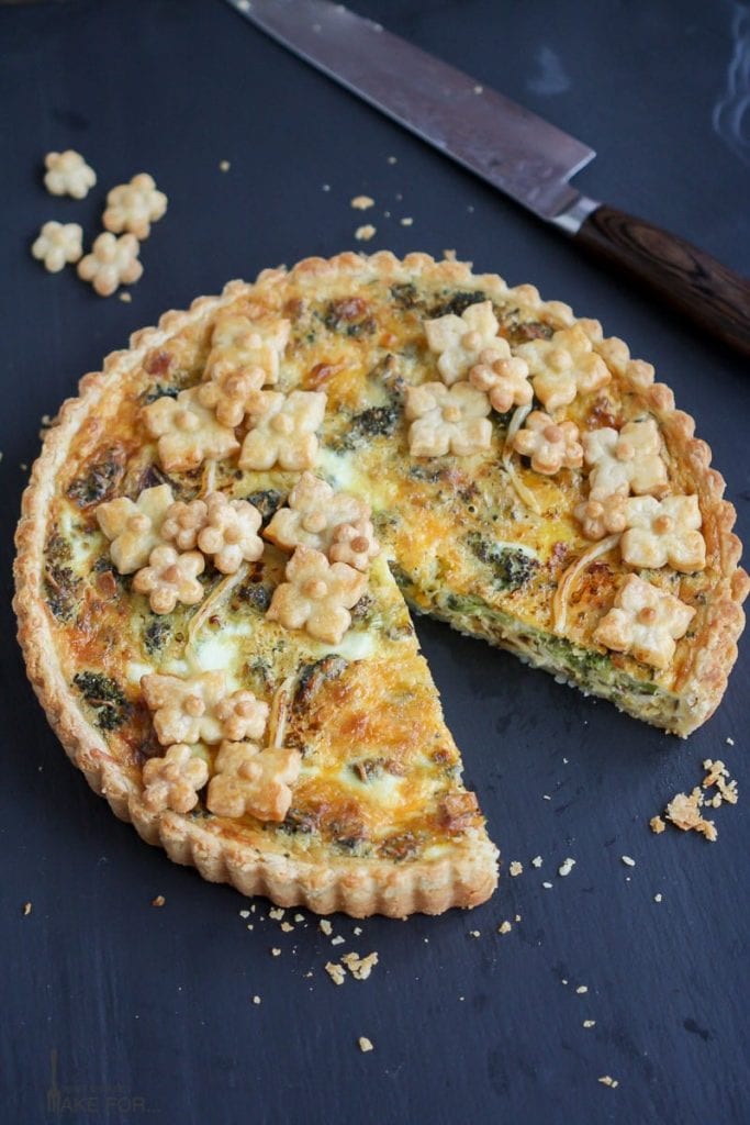Roasted Broccoli Quiche with fluted edges decorated with little pastry flowers with a slice cut out.