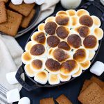 S'mores dip topped with golden brown marshmallows with graham crackers and marshmallows scattered around.