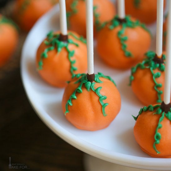 A close up of pumpkin cake pops with sticks up and green vines on the orange cake pops.