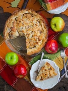 Classic Apple Pie with a large slice on a plate and apples scattered around.