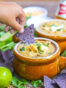 A bowl of white chicken chili topped with sour cream, cheese, and cilantro served with blue corn chips for dipping.