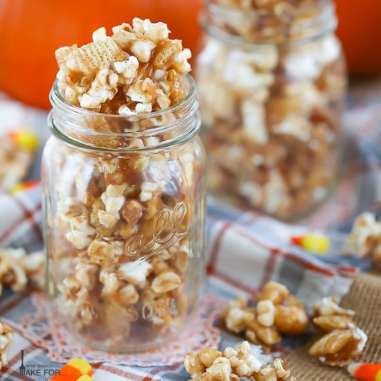 Autumn Caramel Popcorn in a mason jar and scattered around on a plaid towel with candy corn.
