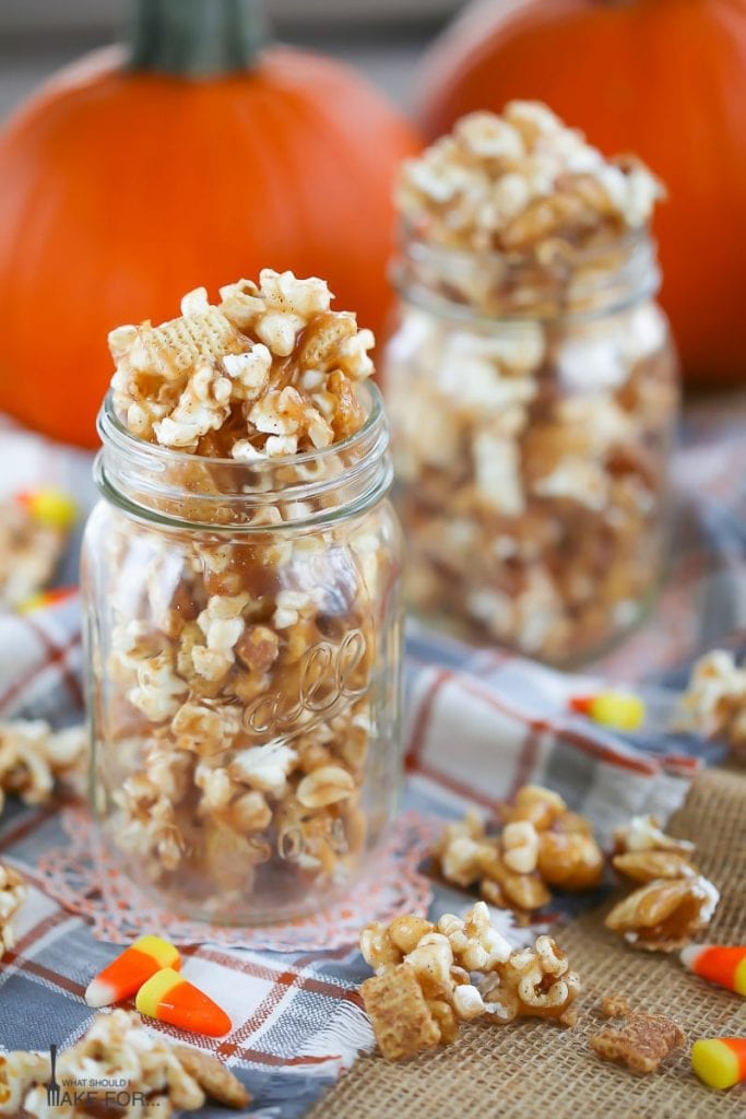 Autumn Caramel Popcorn in glass mason jars on a plaid towel with caramel corn and candy corn scattered around.