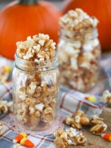 Autumn Caramel Popcorn in glass mason jars on a plaid towel with caramel corn and candy corn scattered around.