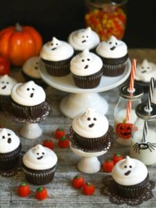 A cute Halloween display of easy ghost cupcakes stacked on a cake plate and cupcake stands with candy pumpkins scattered around.