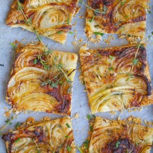 French Onion Tart cut into square slices, golden brown, and scattered with thyme sprigs.