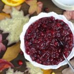 Overhead shot of Orange Cranberry Sauce in a pretty white bowl with fall leaves and fresh cranberries scattered around.