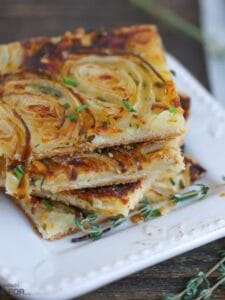 French Onion Tart slices stacked on an appetizer plate with thyme sprigs scattered around.