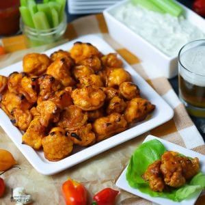 Buffalo Cauliflower Bites with Blue Cheese Dip served on a white square platter with celery stalks and a beer in the background.