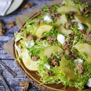Pear Frisée Salad with Candied Walnuts and Goat Cheese served on a round wooden cutting board.