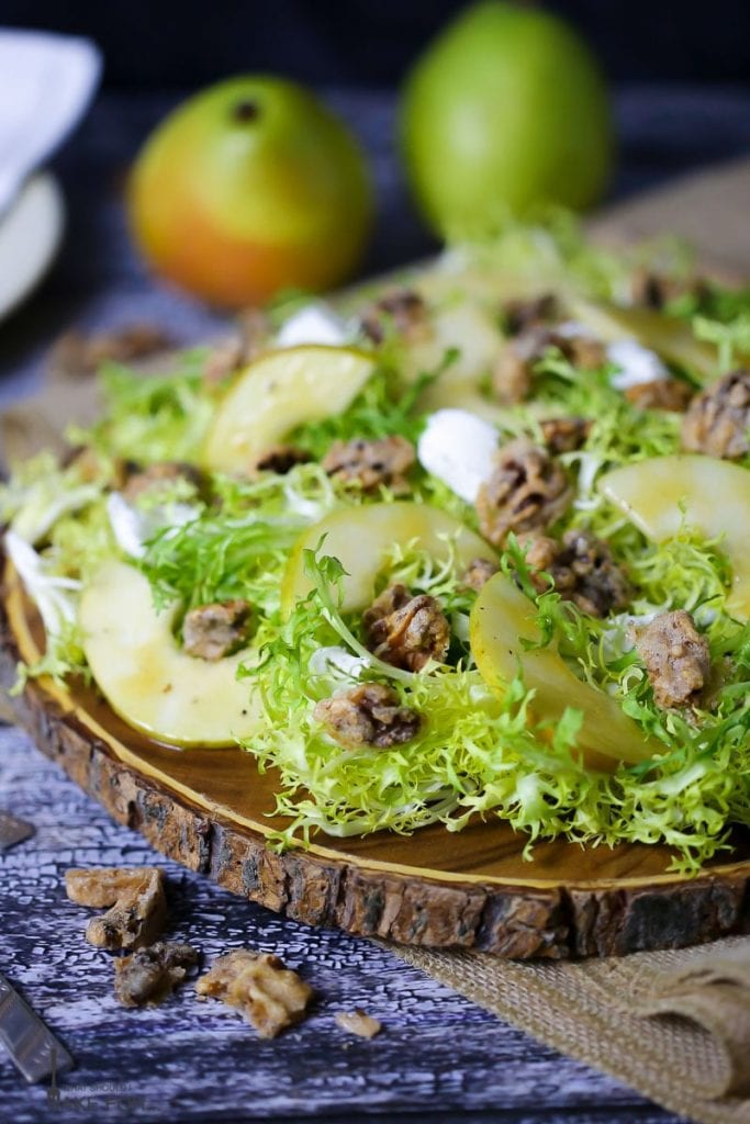 Pear Frisée Salad with Candied Walnuts and Goat Cheese served on a round wooden cutting board with two anjou pears in the background.