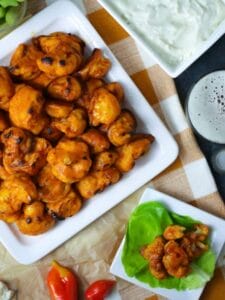 Overhead shot of Buffalo Cauliflower Bites with Blue Cheese Dip with a glass of beer and a serving of buffalo cauliflower on a small square plate.
