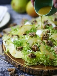 Sherry Vinaigrette being poured over Pear Frisée Salad with Candied Walnuts and Goat Cheese.