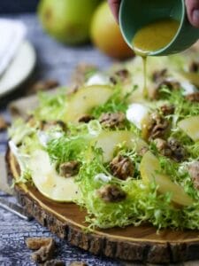 Sherry Vinaigrette being poured over Pear Frisée Salad with Candied Walnuts and Goat Cheese.