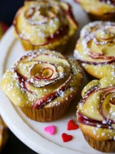 Close up shot of Apple Rose Cupcakes dusted with confectioners sugar and little candy hearts scattered on the plate.