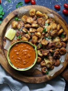 Crispy Tortellini Bites with Creamy Tomato Sauce served on a round wood board with tomato sauce in a small bowl with fresh parsley and grape tomatoes scattered around.