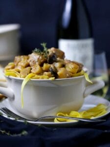Veal and Mushroom Stew piled high in a crock with a noodle hanging over the side.