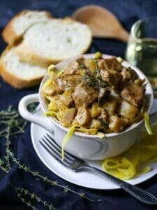 A bowl of Veal and Mushroom Stew garnished with thyme and bread in the background.
