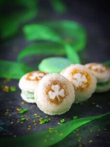 Shamrock Macarons decorated with gold glitter shamrocks and green ribbon in the background.