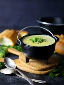 Broccoli Cheese Soup in a crock set on top of wooden cutting boards with two spoons on the table.