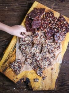A little hand grabbing a piece of one of three types of Toffee Matzo Brittle (aka matzo crack), are piled on top of a wood board.