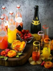 Mother's Day mimosa bar all set up with juices in glass bottles, sparking mimosas in glasses and garnishes scattered around.