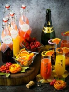 Mother's Day mimosa bar all set up with juices in glass bottles, sparking mimosas in glasses and garnishes scattered around.