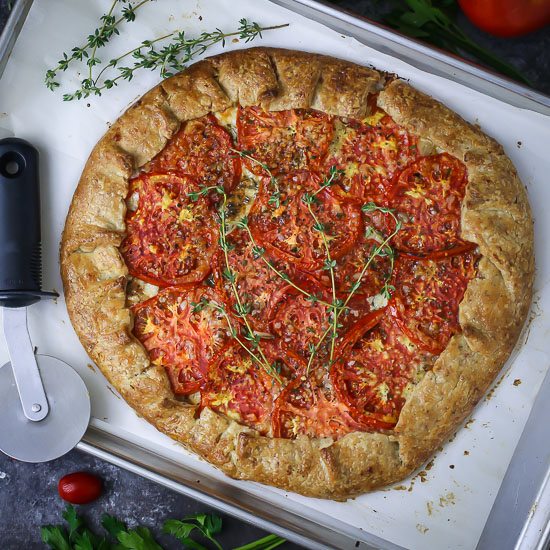 Tomato Galette on a lined baking sheet garnished with fresh thyme sprigs.