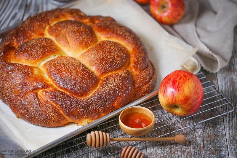 A close up of a golden brown round loaf of apple challah bread served with apples and honey for Rosh Hashanah.