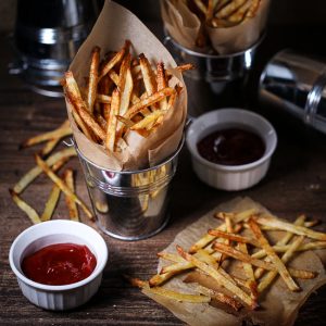 Oven fries in paper-lined metal serving bucket served with spicy sriracha ketchup.