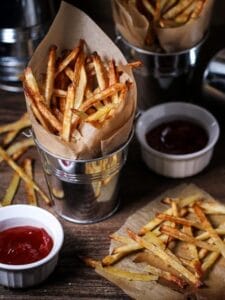 Oven fries in paper-lined metal serving bucket served with spicy sriracha ketchup.