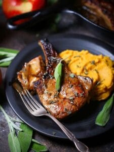 Apple cider pork chop plated with butternut squash mash surrounded by apples and sage.