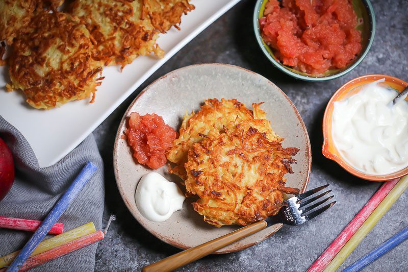 Two Celery Root Latkes on a small plate served with apple sauce and sour cream.