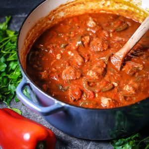 Veal and Peppers braised in tomato sauce in a large pot.