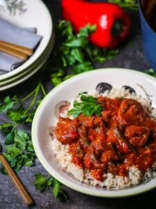 Braised Veal and Peppers in a bowl served over rice with a red pepper in the background.