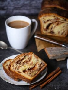 Two slices of Cinnamon Babka on a plate with a cup of coffee next to it.