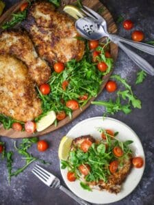 Pork Milanese with Arugula and Tomatoes on an oval wood plate with a serving on a small white plate.
