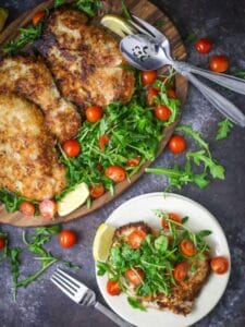 Pork Milanese with Arugula and Tomatoes on an oval wood plate with a serving on a small white plate.