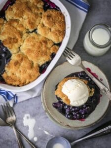 Blueberry Cobbler in the baking dish and on a small serving plate with ice cream.